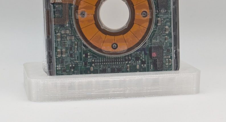 May include: A close-up of a circuit board with a circular, orange component in the center. The circuit board is mounted on a clear, plastic base.