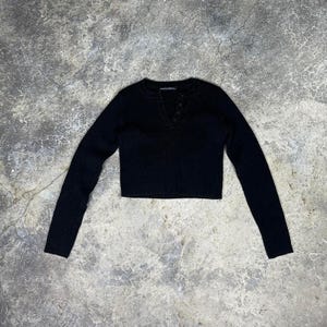 May include: A black long-sleeved crop top with a V-neckline and three buttons. The top is made of a soft material and has a ribbed texture. The sleeves are long and fitted.