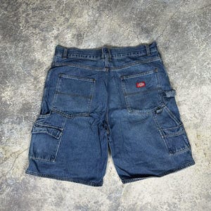 May include: Blue denim shorts with multiple pockets, including cargo pockets on the sides. The shorts have a classic design with a red logo patch on the back pocket. The shorts are made of durable denim material.