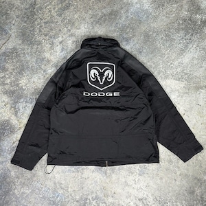 Puede incluir: Chaqueta negra con el logotipo de Dodge en blanco en la espalda. La chaqueta tiene cierre de cremallera y cuello alzado. El logotipo de Dodge presenta una cabeza de carnero. La chaqueta está hecha de un material ligero.