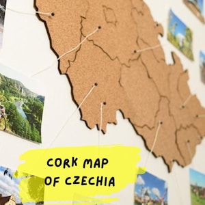 May include: A cork map of the Czech Republic with photos pinned to it. The map is on a white wall with the text "Cork Map of Czechia" written in yellow on a yellow background.