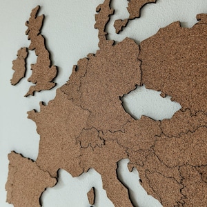Könnte beinhalten: Eine Wandkarte von Europa aus braunem Korkmaterial. Die Karte zeigt lasergeschnittene Umrisse einzelner Länder mit deutlichen Grenzen und stellt die geografischen Formen von Nationen wie den Britischen Inseln, Frankreich und Spanien dar.
