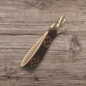 May include: A brown and beige leather keychain with a gold metal clasp. The leather has a repeating pattern of brown and beige flowers.