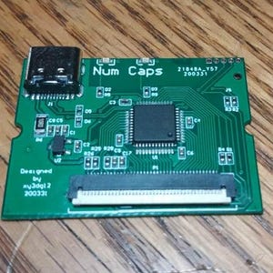 Könnte beinhalten: Eine grüne Leiterplatte mit dem Text "Num Caps" und "21848A-Y57 200331" darauf gedruckt. Die Platine hat einen schwarzen HDMI-Stecker und einen schwarzen Flachbandkabel-Stecker. Der Text "Designed by xy3dg12 200331" ist in der linken unteren Ecke der Platine gedruckt.