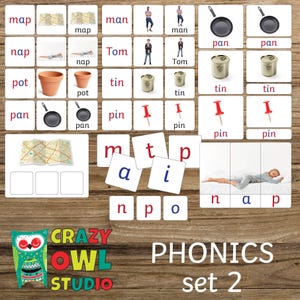 Op de afbeelding: Educatieve phonics flashcards met woorden als "map", "man" en "pan". De set bevat afbeeldingen van objecten en mensen, samen met lettertegels om te spellen. Het "Crazy Owl Studio" logo en de tekst "PHONICS set 2" zijn ook zichtbaar.
