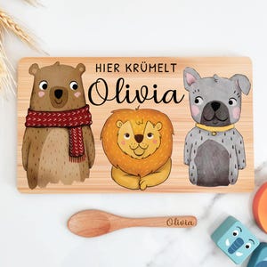 May include: A wooden cutting board with a bear, lion, and dog illustration. The board is personalized with the name "Olivia" and the text "Hier Kr&uuml;melt Olivia".