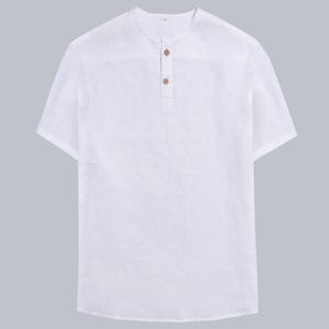 Puede incluir: Camisa blanca de manga corta con cuello mao y tres botones de madera. La camisa está hecha de una tela ligera, perfecta para el clima cálido. La camisa tiene un corte relajado y es adecuada para uso casual.