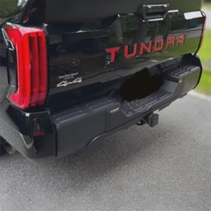 May include: Black truck rear with red "TUNDRA" lettering. The truck has a black bumper and red tail lights. The image shows a 4x4 emblem.
