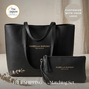May include: A black textured tote bag and a matching zippered clutch with a wrist strap. Both items feature the gold-printed text Isabella Dupont Real Estate. The tote has two shoulder straps, and the clutch includes a decorative tassel detail.