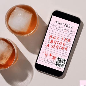 May include: Two glasses of amber-colored liquid with ice cubes sit next to a smartphone. The phone displays a "Guest Check" with the text "BUY THE BRIDE A DRINK" in red. The background is a light pink.