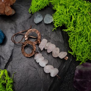 May include: A pair of copper earrings with hammered circles and pink rose quartz chips hanging from them.