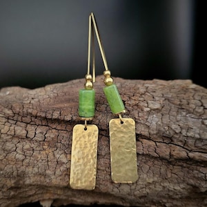 Op de afbeelding: Een paar gouden oorbellen met groene steentjes. De oorbellen hebben een gehamerde gouden rechthoekige hanger en een groene steenkraal.
