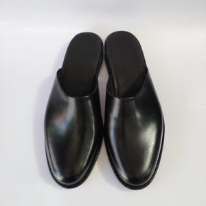 以下が含まれることがあります： 黒い革のスリッポンシューズのペア。靴は丸いつま先と低いヒールが付いています。アッパーは滑らかで光沢があり、ソールは暗いです。靴は簡単に着脱できるように設計されています。