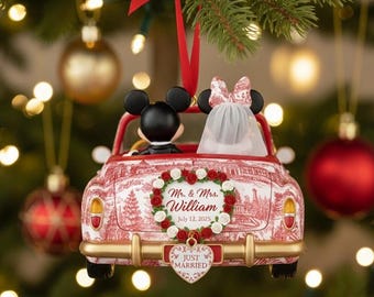 May include: A red and white patterned car ornament featuring Mickey and Minnie Mouse figures, a heart-shaped wreath with the text Mr. & Mrs. William July 13, 2025, and a heart-shaped license plate that reads Just Married, all suspended by a red ribbon.