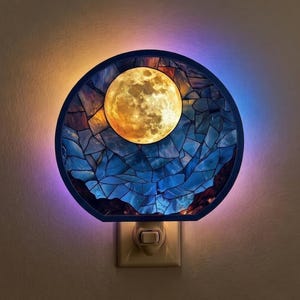 Op de afbeelding: Decoratief nachtlampje met een volle maan ontwerp. De maan is helder geel-oranje, tegen een mozaïek van blauwe, oranje en bruine vormen. Het nachtlampje heeft een donkerblauw frame en is aangesloten op een stopcontact.