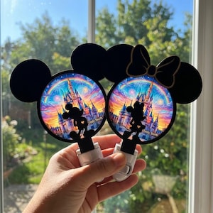 Könnte beinhalten: Zwei kreisförmige Nachtlichter mit schwarzen Mickey-Maus-Ohren-Silhouetten. Das linke Licht zeigt eine Mickey-Silhouette und den Text Cody Smith. Das rechte Licht zeigt eine Minnie-Silhouette mit Schleife und den Text Emily Smith. Beide zeigen ein farbenfrohes Schloss, einen Regenbogen und ein Feuerwerk.