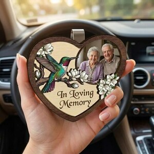 Peut inclure: Charm de voiture en bois en forme de cœur avec une illustration de colibri et le texte "In Loving Memory". Le charme présente une photo d'un couple de personnes âgées. Le colibri est vert, bleu et rouge, perché sur une branche fleurie.