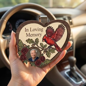 May include: Heart-shaped wooden car charm with the text "In Loving Memory." Features a red cardinal bird, a photo, and floral accents. Includes a metal clip for hanging.
