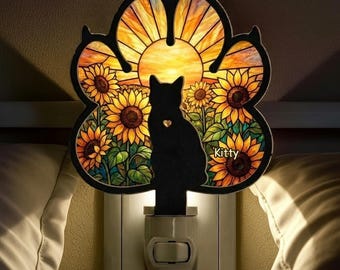 以下が含まれることがあります： 黒い猫のシルエットとハート型の切り抜きが特徴の肉球型ナイトライト。背景には明るい太陽の下に咲く黄色いヒマワリの鮮やかなシーンが描かれています。Kittyという文字が白でプリントされています。