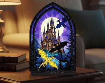 May include: A decorative night light with a stained-glass effect, depicting a castle scene with dragons. The design features a purple sky, a full moon, and a detailed castle. Two dragons, one yellow and one black, are shown in flight, framed in black.