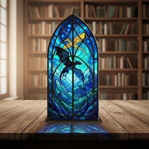 May include: A stained glass panel with a dragon design. The panel has a blue background with a mountain landscape and dragons in flight. The dragons are black and gold. The panel is set on a wooden table.