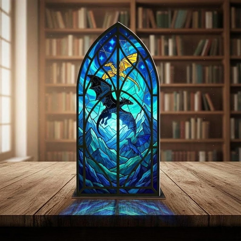 May include: A stained glass panel with a dragon design. The panel has a blue background with a mountain landscape and dragons in flight. The dragons are black and gold. The panel is set on a wooden table.