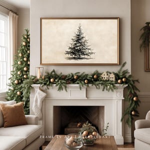 Puede incluir: Una impresión en blanco y negro enmarcada de un árbol de Navidad cuelga sobre una chimenea decorada con guirnaldas, adornos dorados y casitas. Un árbol de Navidad con adornos dorados está a la izquierda. El texto "FRAME TV ART | MERRYVUEART" está en la parte inferior.