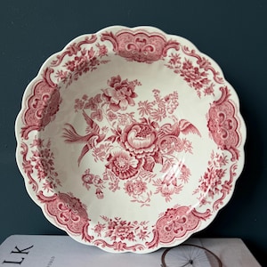 Può includere: Una ciotola da portata bianca e rossa a motivi floreali con bordo smerlato. La ciotola presenta un design dettagliato di fiori e uccelli. Il bordo ha un bordo decorativo. La ciotola è probabilmente in ceramica o porcellana.