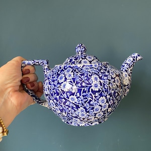Può includere: Teiera a fantasia floreale blu e bianca. La teiera ha un beccuccio curvo, un manico e un coperchio con un pomello decorativo. Il motivo floreale è un disegno ripetuto di piccoli fiori bianchi su sfondo blu.