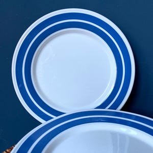 Puede incluir: Dos platos de cerámica blanca con rayas azules alrededor del borde. Los platos están apilados uno encima del otro.