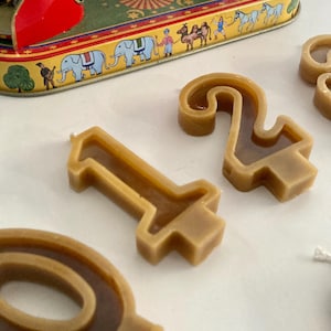 Puede incluir: Un juego de cuatro velas de cera marrón con forma de los números 1, 2, 0 y 9. Las velas están sobre una superficie blanca.