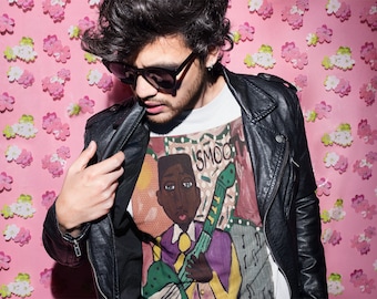 May include: A man wearing a black leather jacket over a white t-shirt with a colorful graphic print of a person playing a guitar. The graphic includes the word "SMOOTH".