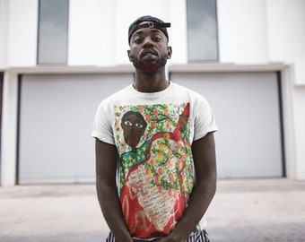 May include: A white t-shirt with a colorful graphic print of a person playing a musical instrument. The graphic features a person with large eyes, a green shirt, and a red musical instrument with a floral design.