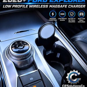 May include: A low profile wireless MagSafe charger designed for 2020+ Ford Explorer vehicles. The black circular charging pad is mounted within the center console cup holder, positioned next to the rotary gear shift dial and parking brake controls.