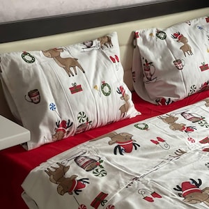 May include: White Christmas-themed bedding set with a red base. The set features reindeer, candy canes, wreaths, and gift box patterns. The pillowcases and duvet cover are decorated with festive holiday designs.