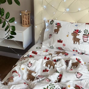 Puede incluir: Juego de cama blanco con temática navideña que presenta un patrón repetido de renos con gorros de Papá Noel, regalos envueltos y bastones de caramelo. El juego incluye una funda de almohada y una funda nórdica, ideal para la temporada navideña.