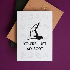 May include: A white card with a black and white illustration of a witch's hat and the text "You're just my sort". The card is surrounded by a border of small black and white illustrations of animals and objects.
