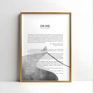 Può includere: Stampa incorniciata di "DUNE" di Frank Herbert. L'opera presenta testo dal romanzo e un'illustrazione in scala di grigi di un paesaggio. La cornice è dorata.