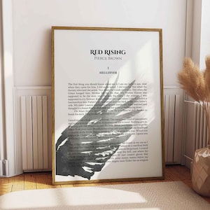 May include: A framed print of the book "Red Rising" by Pierce Brown. The text is displayed in a clean, modern font. A black and white illustration of a bird's wing is at the bottom of the page. The print is in a wooden frame.