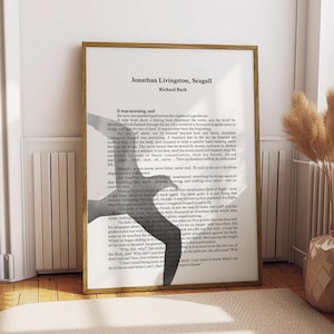 May include: A framed print of "Jonathan Livingston Seagull" by Richard Bach. The text is in black font on a white background, with a silhouette of a seagull. The frame is a light brown color.