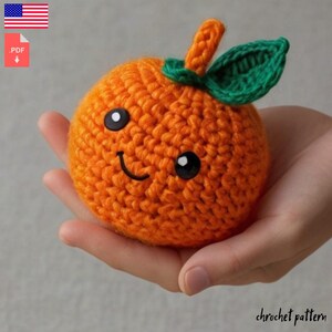 Può includere: Schema a uncinetto per un simpatico giocattolo amigurumi a forma di arancia. L'arancia è arancione e ha una foglia verde in cima. Ha un viso sorridente con occhi neri.