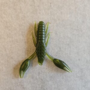 May include: A green plastic crawfish lure with a segmented body, small antennae, and two large claws. The lure is designed to mimic a crawfish and is used for fishing. The lure is made of a soft, flexible plastic material.