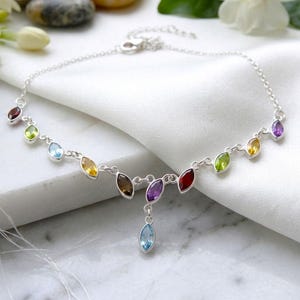 Pode incluir: Uma tornozeleira de corrente prateada com uma série de pedras preciosas multicoloridas de corte marquise dispostas ao longo da corrente, com um pingente central pendurado também cravejado com uma pedra azul clara de corte marquise e fecho lagosta.
