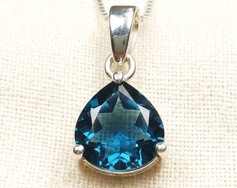 Puede incluir: Un colgante de topacio azul de Londres en forma de pera y facetado, montado en un engaste de garras de plata pulida. La piedra preciosa presenta un tono azul intenso y está suspendida de una delicada cadena de plata de eslabones.