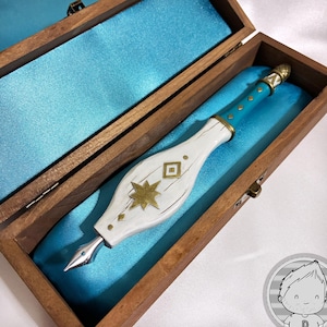 May include: A dip pen with a white, wood-textured handle featuring a gold star and diamond inlay, a teal grip with gold accents, and a silver metal nib. The pen rests inside a rectangular wooden box lined with bright teal satin fabric.
