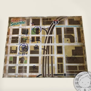 Puede incluir: Un mapa del centro de Seattle con nombres de calles y una autopista. Se han añadido notas y símbolos manuscritos, incluyendo una anotación de "no gas". El mapa está sobre una superficie blanca.