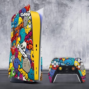 Puede incluir: Una consola de juegos amarilla, blanca y negra con una piel colorida de estilo de dibujos animados que presenta palabras como "Love", "Peace" y "Party". La consola está junto a un mando a juego con el mismo diseño.