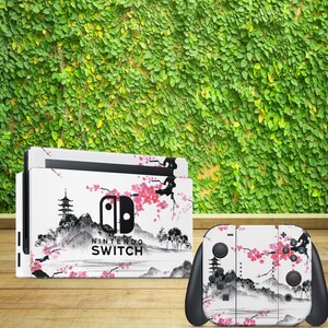 Könnte beinhalten: Eine weiße Nintendo Switch Konsolen- und Controller-Haut mit einem japanisch inspirierten Design in Schwarzweiß, das Kirschblüten, eine Pagode und Berge zeigt. Der Text "Nintendo Switch" ist auf der Konsolenhaut aufgedruckt.