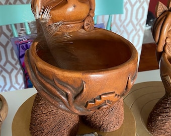May include: A brown ceramic planter shaped like a woman with a bowl on her head. The planter has a textured surface and a small amethyst crystal resting on the base.