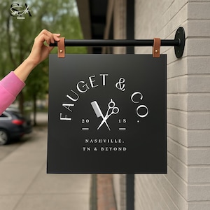 Puede incluir: Letrero cuadrado negro para Faucet & Co. con texto blanco, un peine y un gráfico de tijeras. El letrero está suspendido por una barra negra y correas de cuero marrón. El texto dice "Nashville, TN & Beyond".